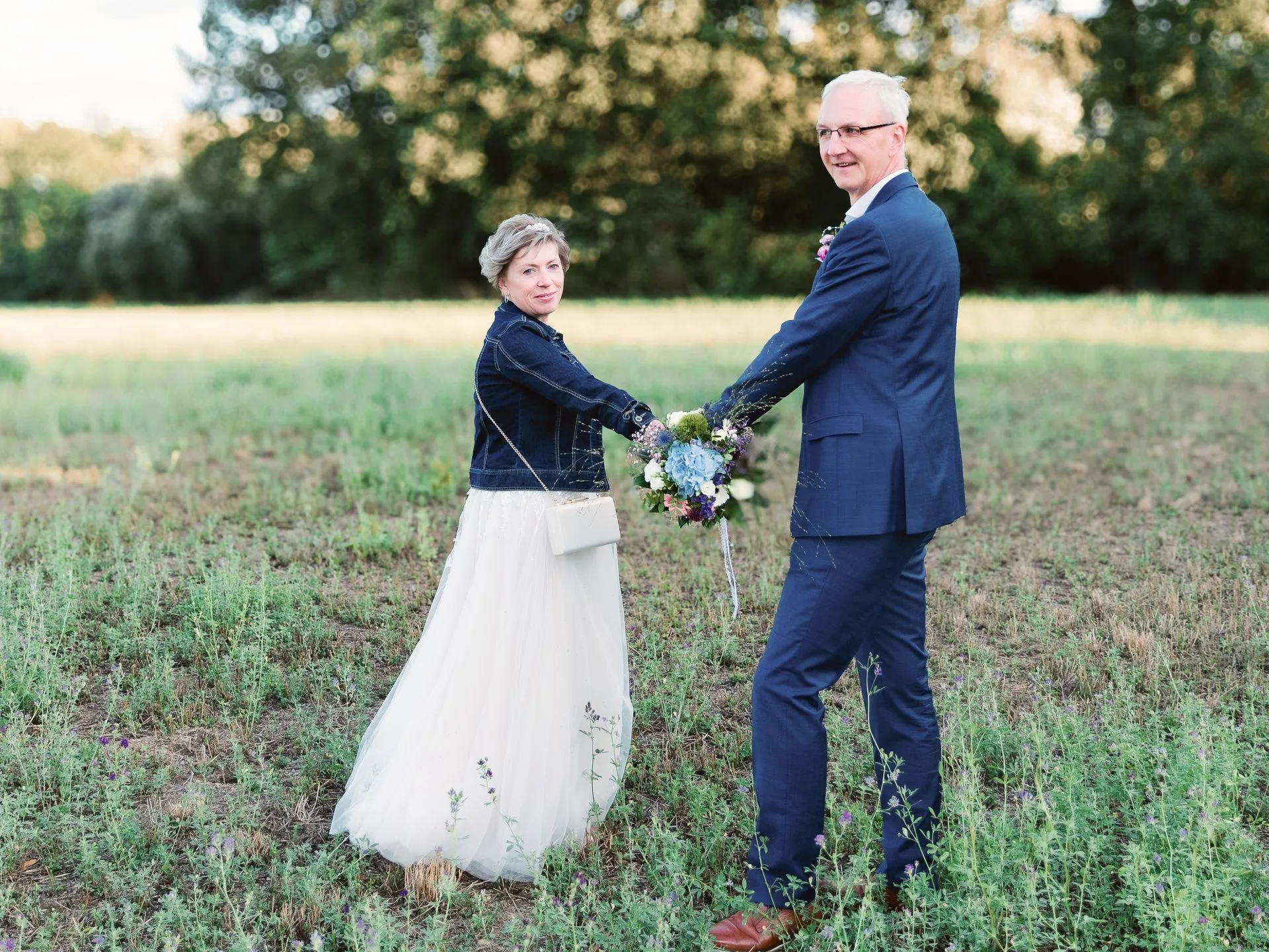 Brautpaar Hand in Hand auf einer Wiese im Abendlicht